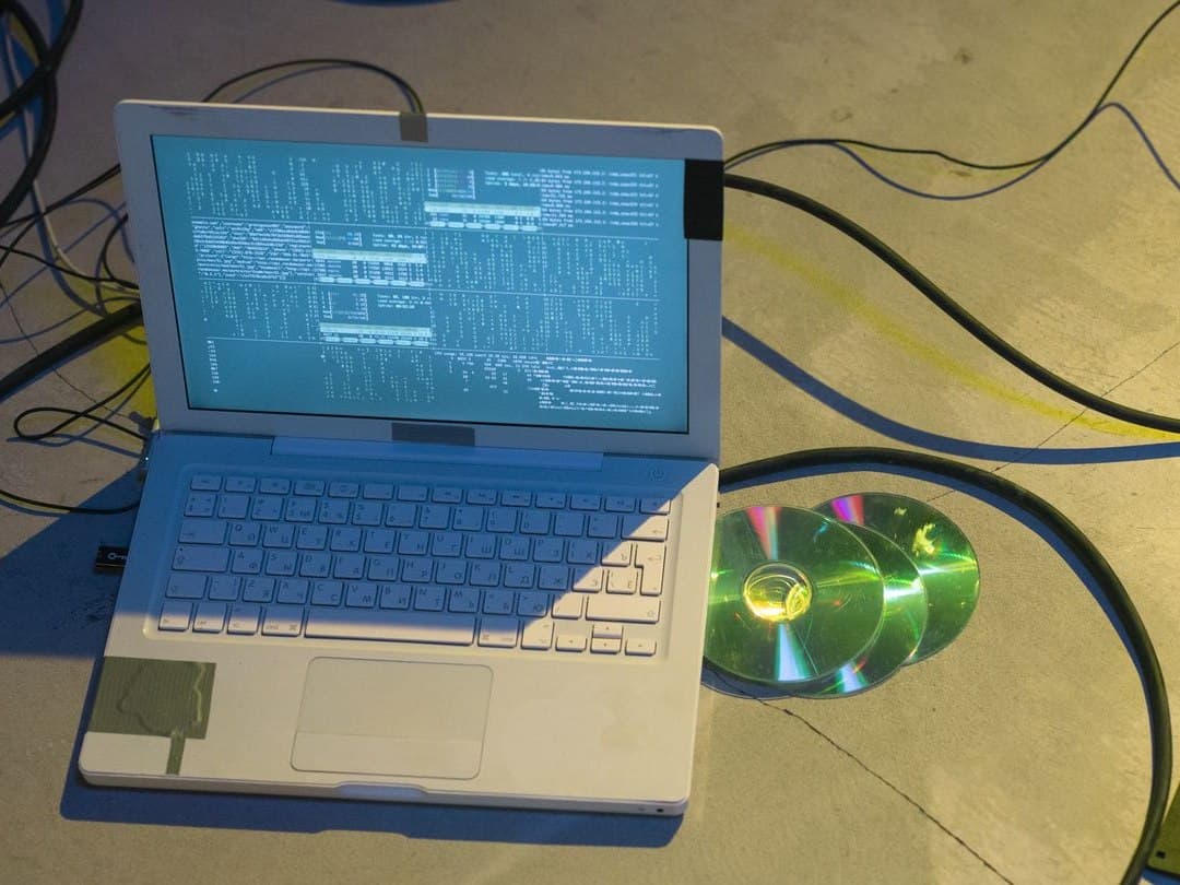 Old laptop on a concrete floor with tangled cables, discs and a floppy drive